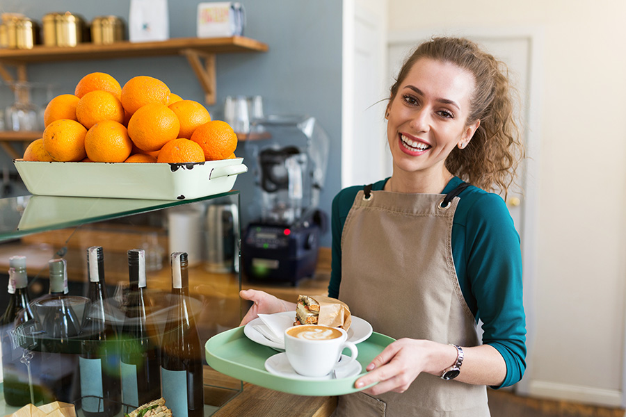 Business Insurance - Woman Wearing a Smok Getting Ready to Serve a Plate of Coffee and Sandwich at a Cafe
