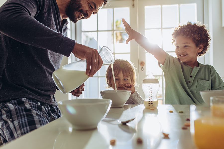 Personal Insurance - Smiling Father Pouring Milk in to Bowls for Breakfast for His Two Children